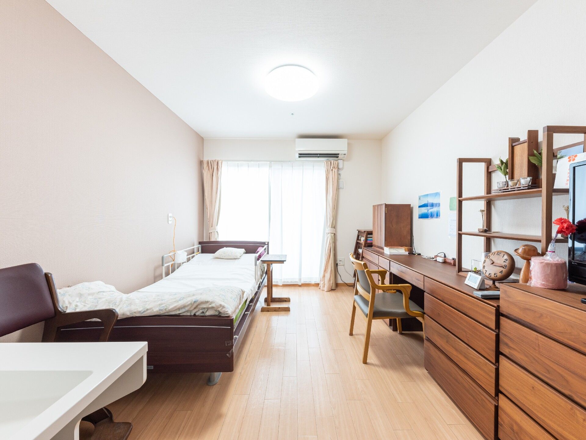 壁側には介護用のベッドがあり、足元には洗面台が設置されている。部屋の窓は大きく、エアコンも完備されている。
