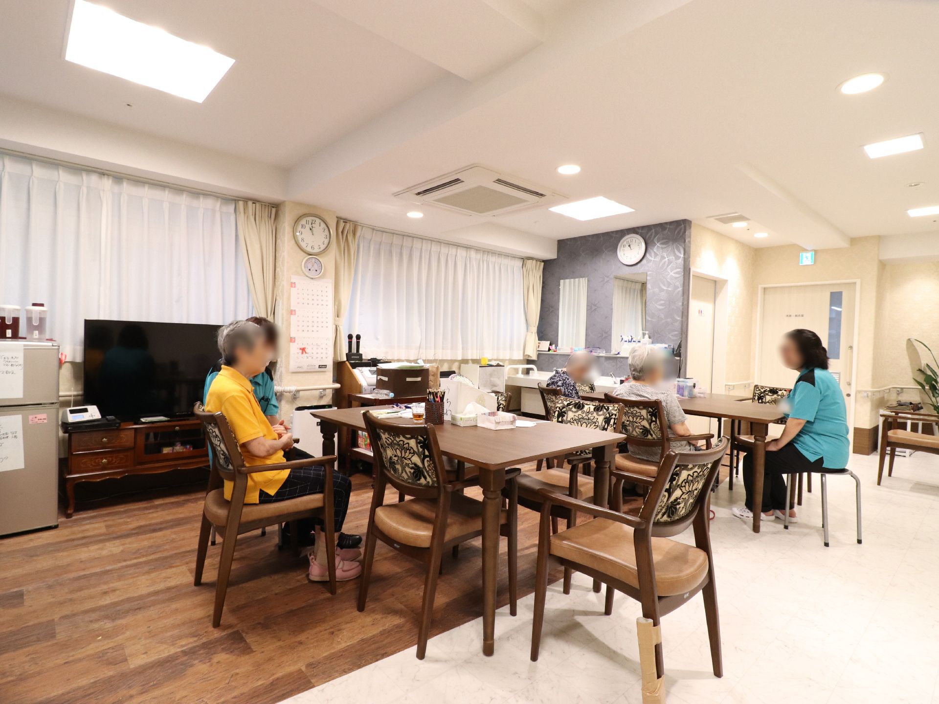 大きな窓が壁側に幾つかあり、手摺が設置されている。大きいテレビに冷蔵庫、テーブルと椅子が置かれている。