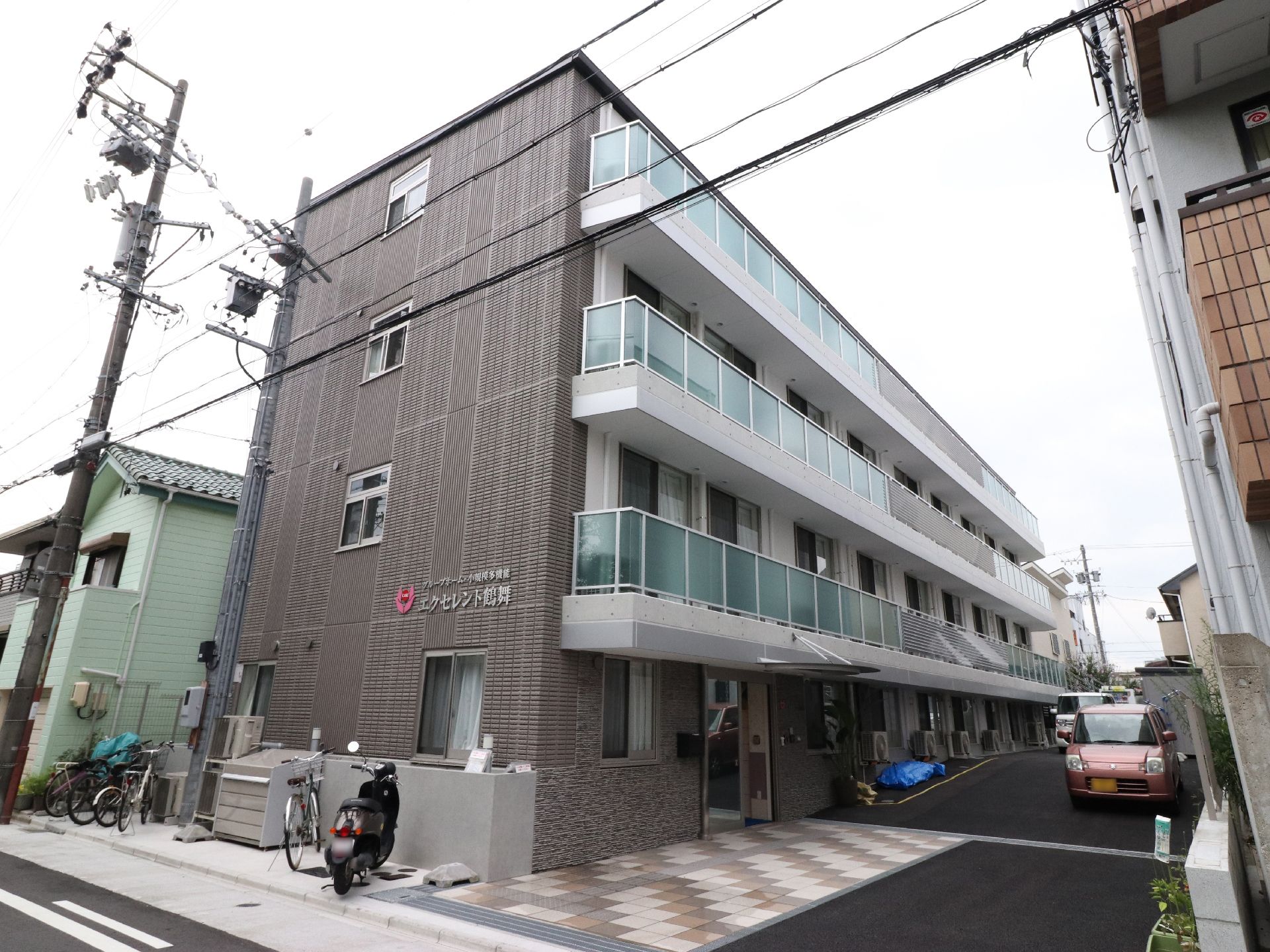 地上4階立て。建物の脇に自転車やバイクが停められるスペースがある。車は建物の前に停めてある。2階から4階はベランダが付いている。