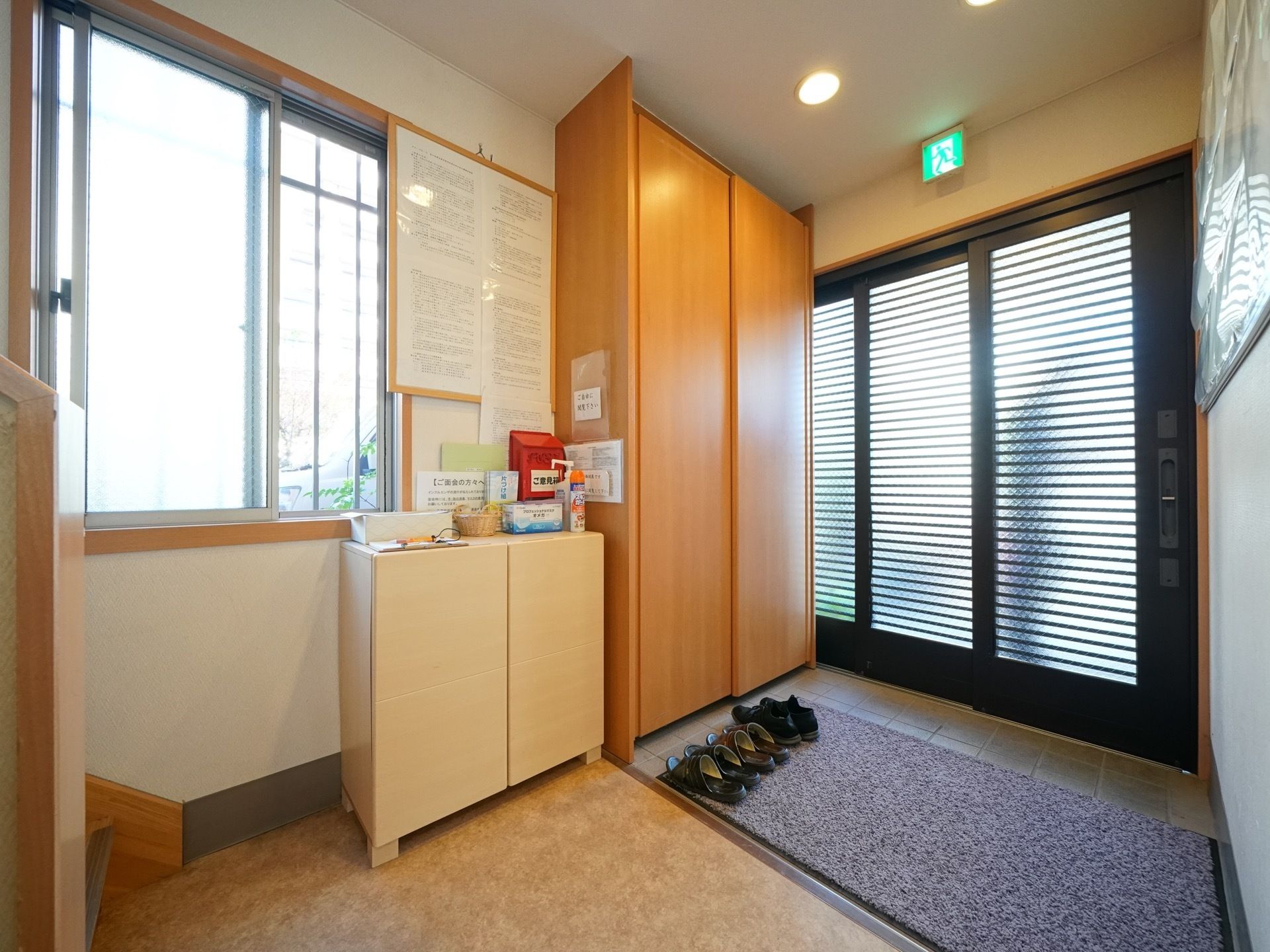 間口の広い横開きの扉である。用途の異なる下駄箱が２つ設置されており、大きな窓がある。目の前に階段が続いている。