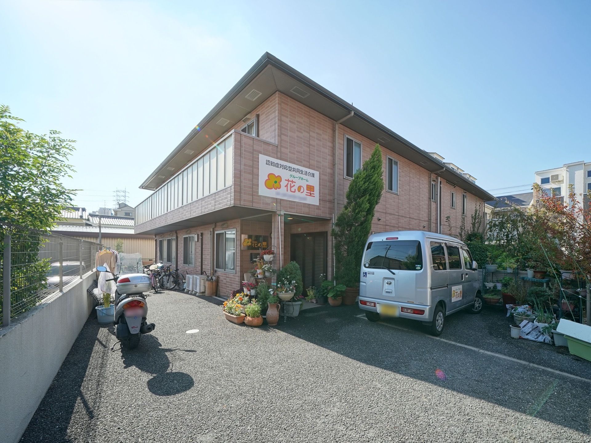 入口にはたくさんの草花が置かれている。２階のバルコニーは、たっぷりの日差しを受けている。駐車場、駐輪場が完備されている。