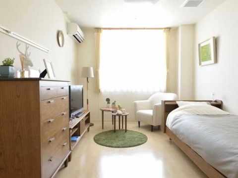 緑色の小さな丸形のカーペットを敷いた、木製家具と白を基調とした北欧風の居室