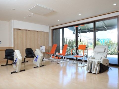 マッサージチェアやリハビリ器具が並ぶ、ガラス張りのリハビリルーム