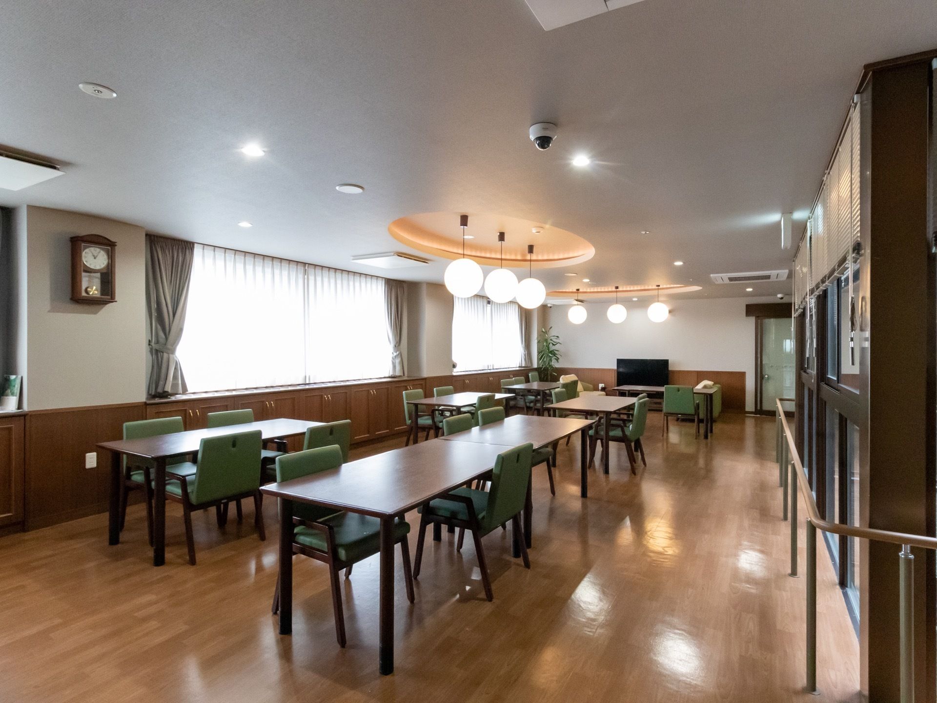 濃い茶色の机には、渋みのあるグリーンの座面と背もたれがある椅子がセットされている。３つのボール型が並んだ照明が付いている。