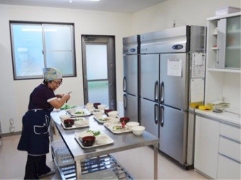 業務用の大きな冷蔵庫がある調理室で、食事の盛り付けをする女性の調理員