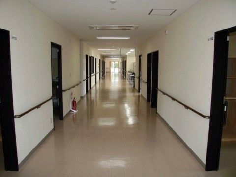 広々とした廊下が手前から奥まで続いている。両側に居室のドアが並んでおり、その間には手すりが取り付けられている。