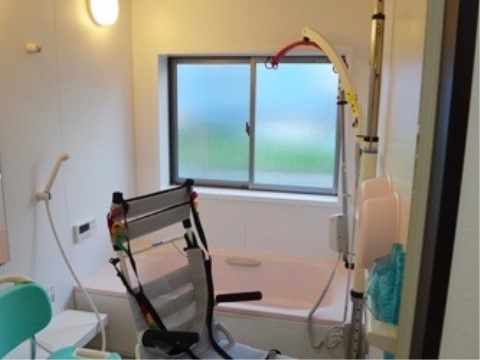 窓からの陽光が明るい浴室。車いす型のシャワーチェアが置かれており、浴槽のところにはリフト浴の装置が用意されている。