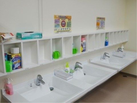手洗い石けんとペーパータオルの置かれた洗面台が４つ並んでいる。上は棚になっており、コップや入れ歯洗浄剤が置かれている。