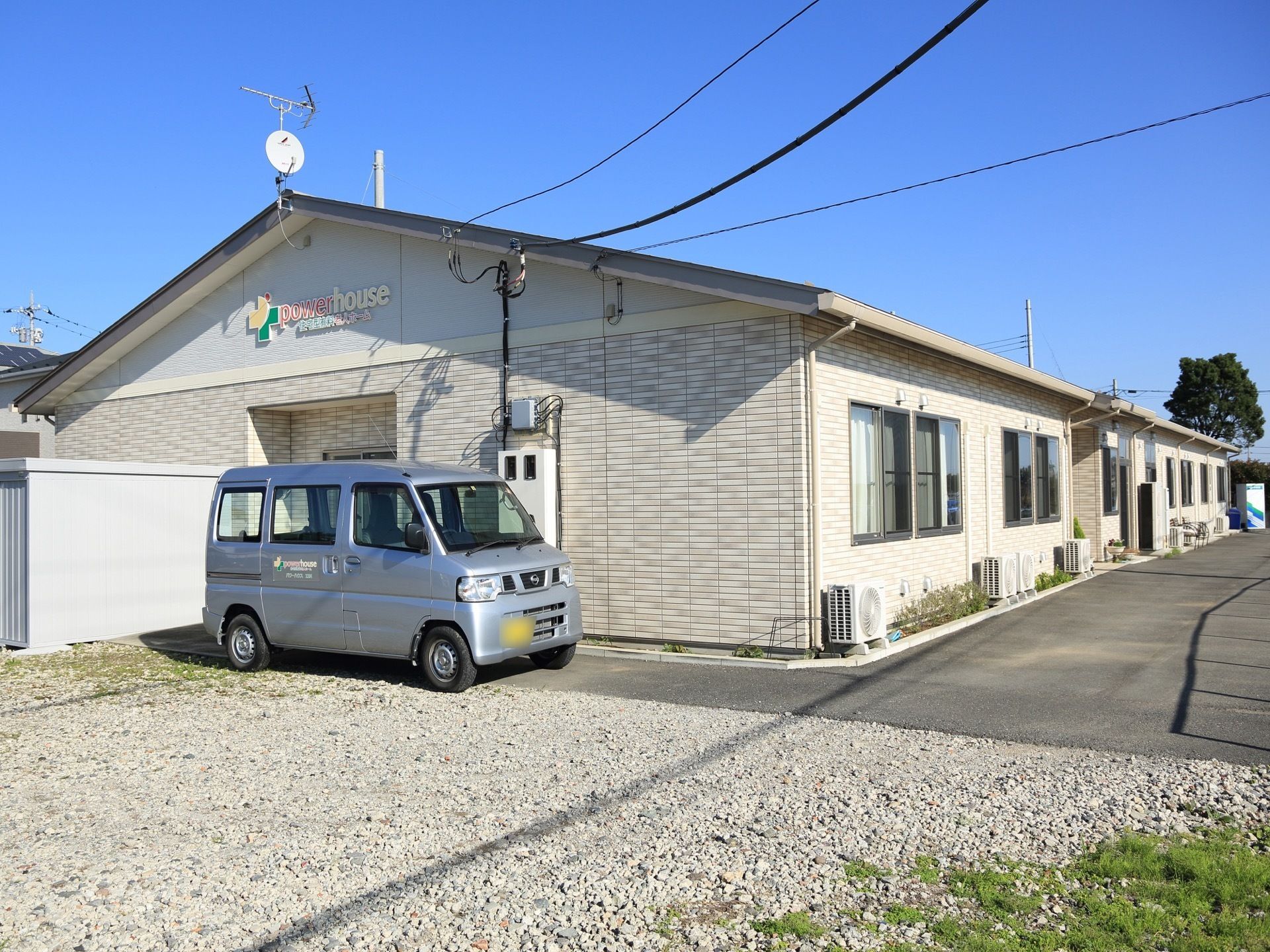 建物の周りには広いスペースがある。玄関の前には施設の車が停まっている。建物の奥には自動販売機がある。