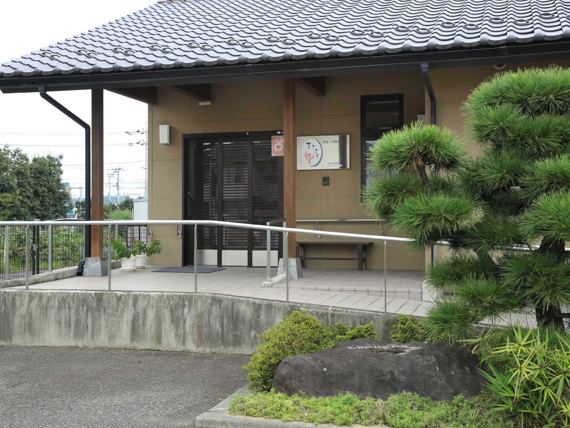 大きな庭石が置かれ、松などが植樹されている。日本家屋風の建物である。スロープがある。玄関口に鉢植えが2つある。