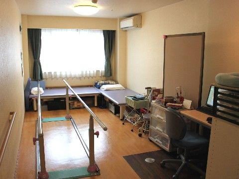 歩行バーやベッド、パソコンなどが置かれたこぢんまりとしたリハビリルーム