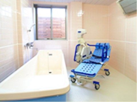 白のタイルの壁と床の浴室である。青色のストレッチャーと機械浴槽がある。寝たきりの入居者様でも安全に入浴することができる。