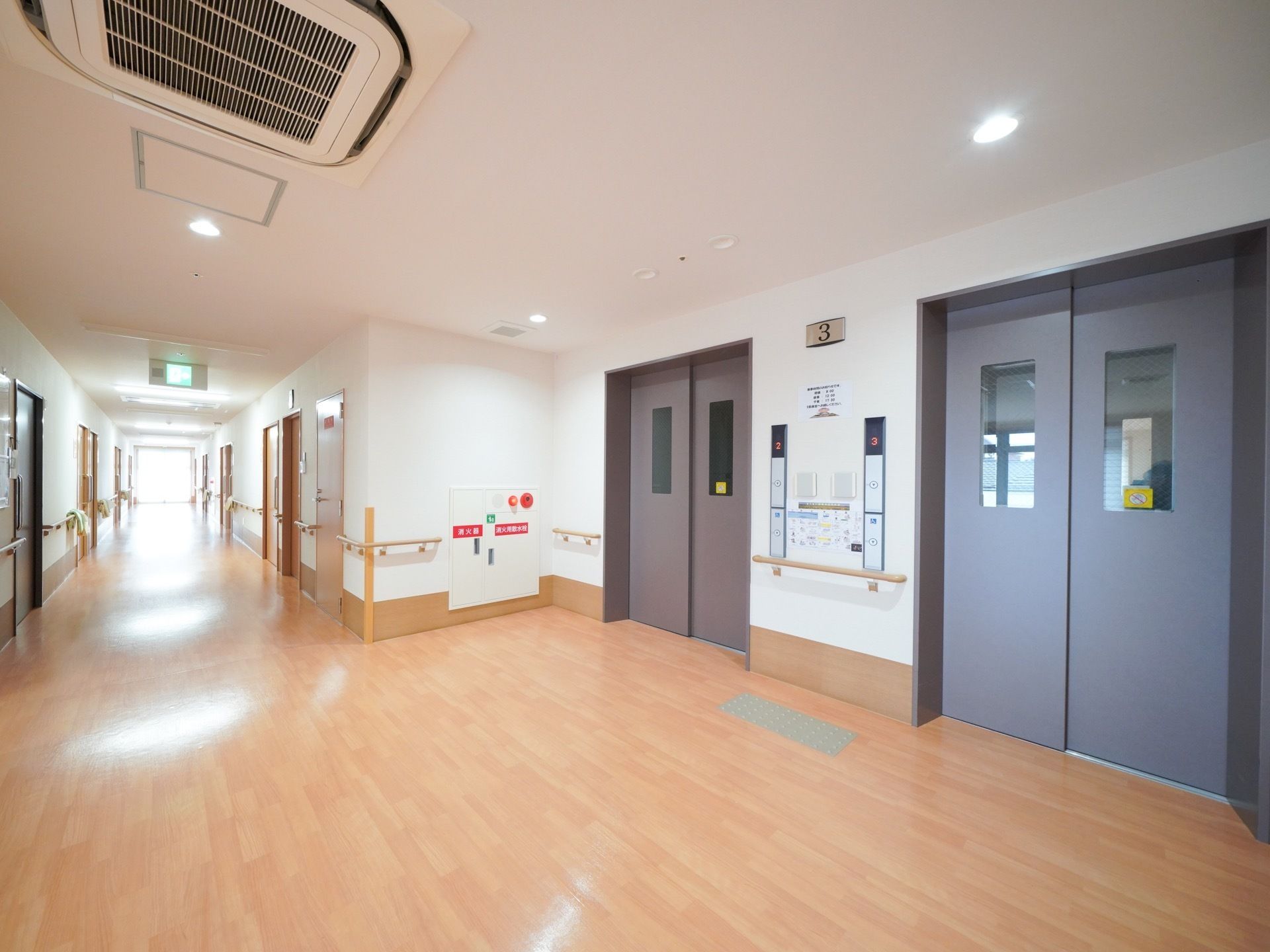 暗色系のシックなエレベーターが２基完備されている。壁には、階を表すプレートが貼られている。手すりもある。