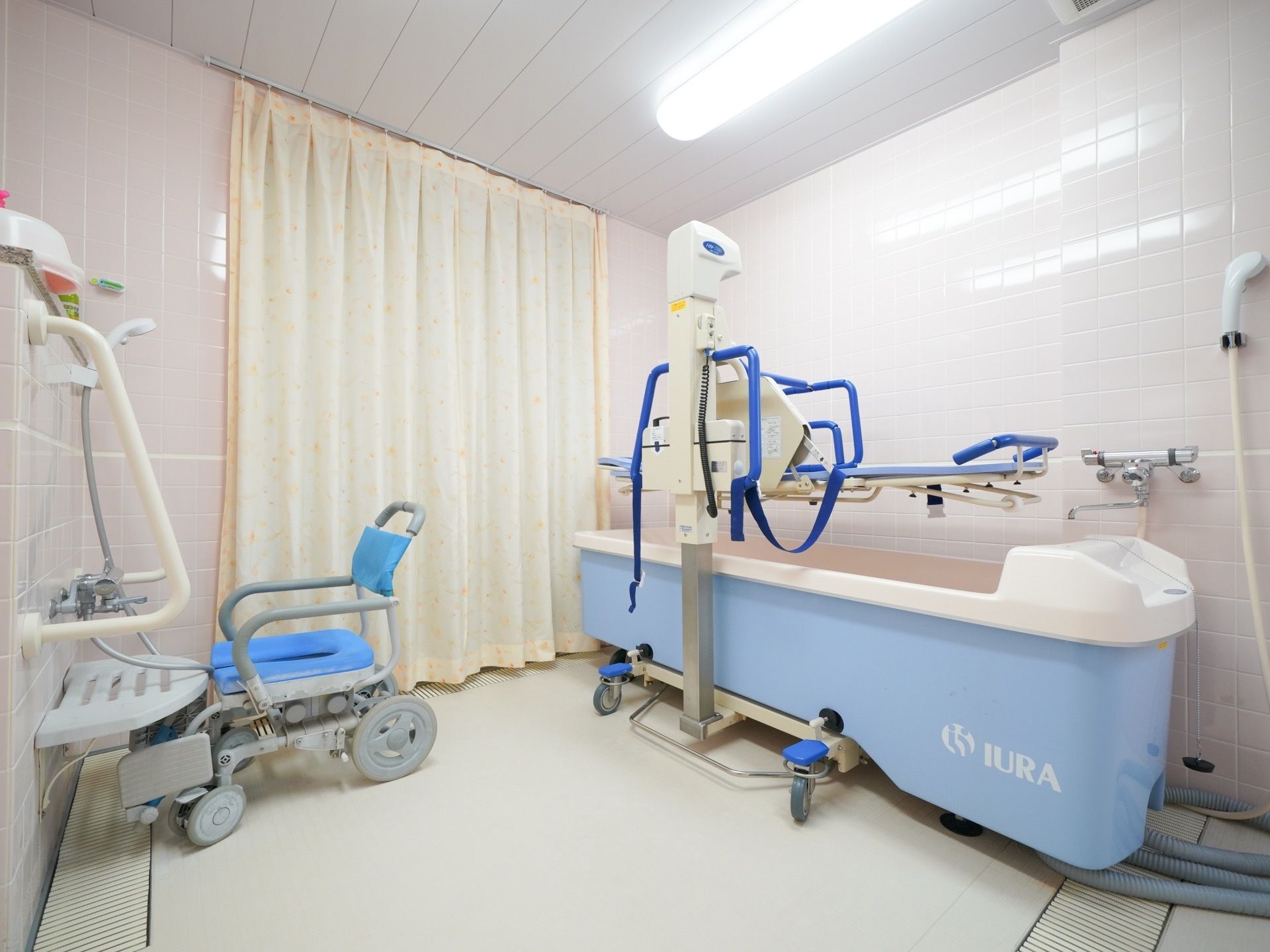 ストレッチャータイプの機械浴室を完備している。壁色は淡いピンク色であたたかみがある。カーテンも設置されている。