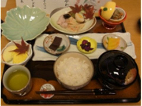 お盆に乗せられた和食。紅葉の葉が飾られ、小鉢に野菜や果物の料理が盛り付けてある。