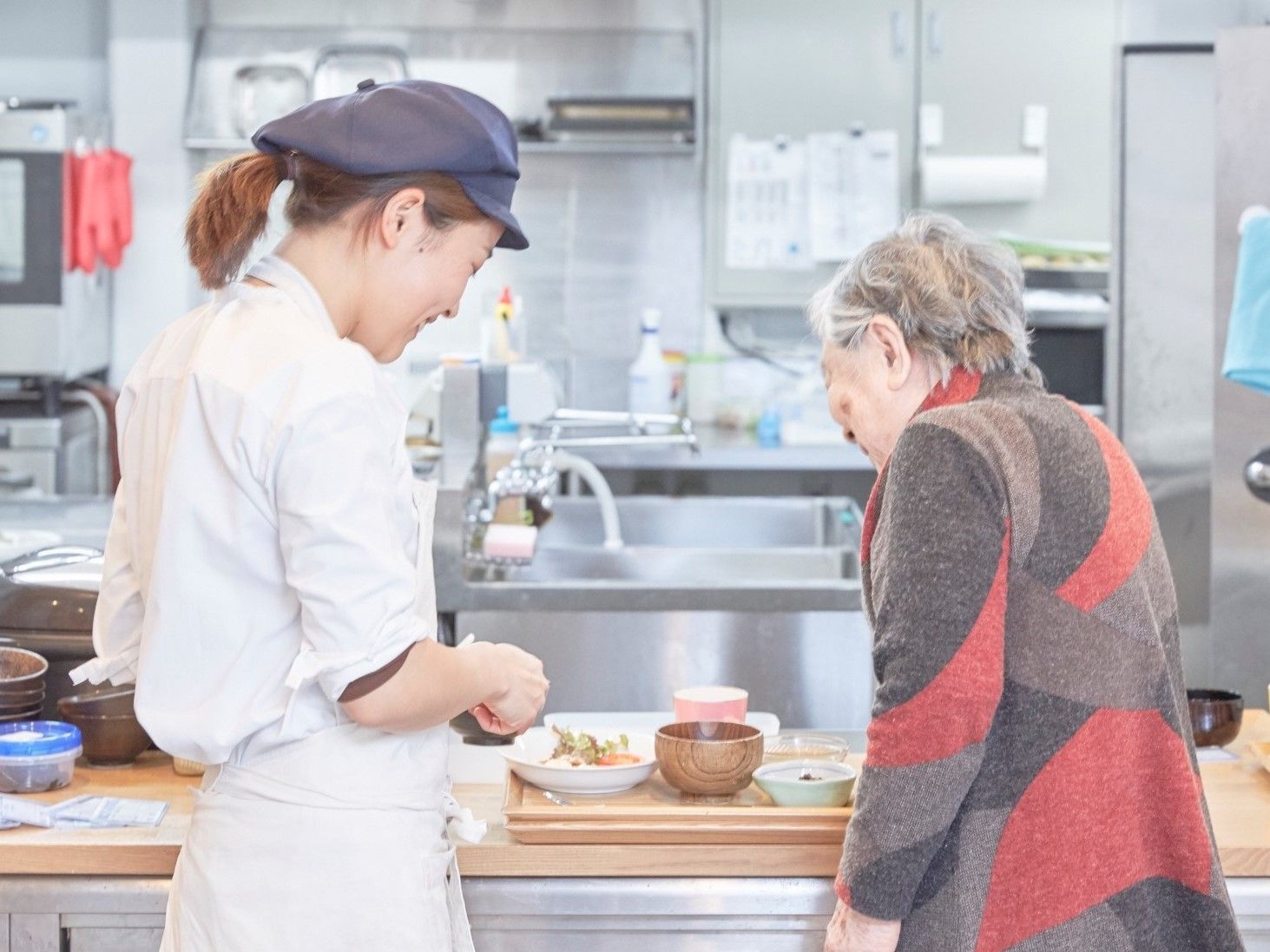 配膳された食事をのぞき込むご年配の女性と帽子をかぶった女性スタッフ