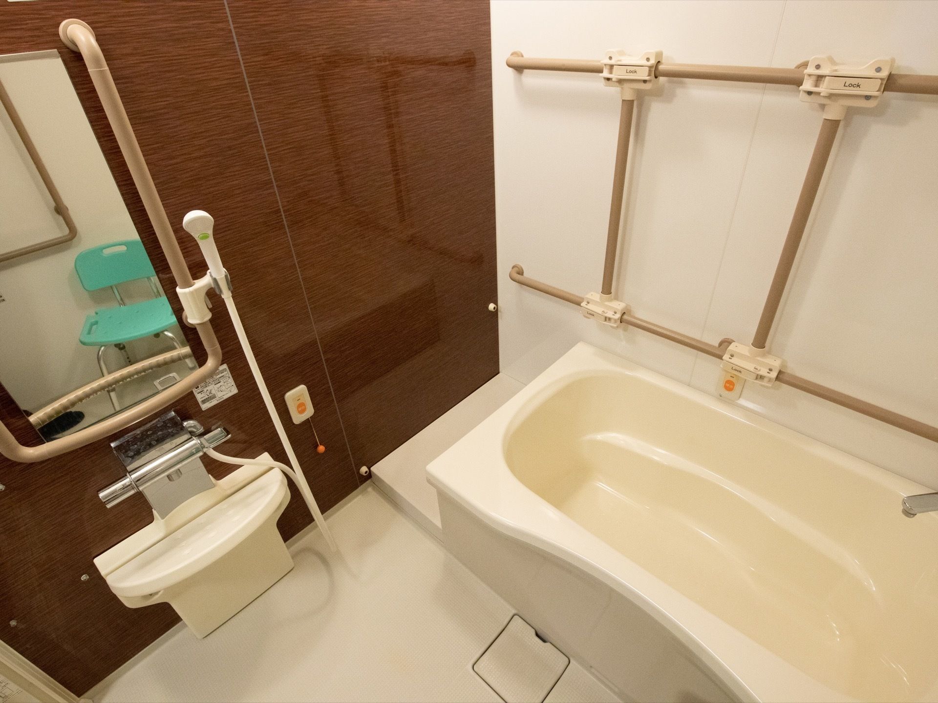 手すりや緊急時呼び出しベルが各所に備わっている個浴用の浴室である。洗い場には背もたれ付きの椅子が置かれている。