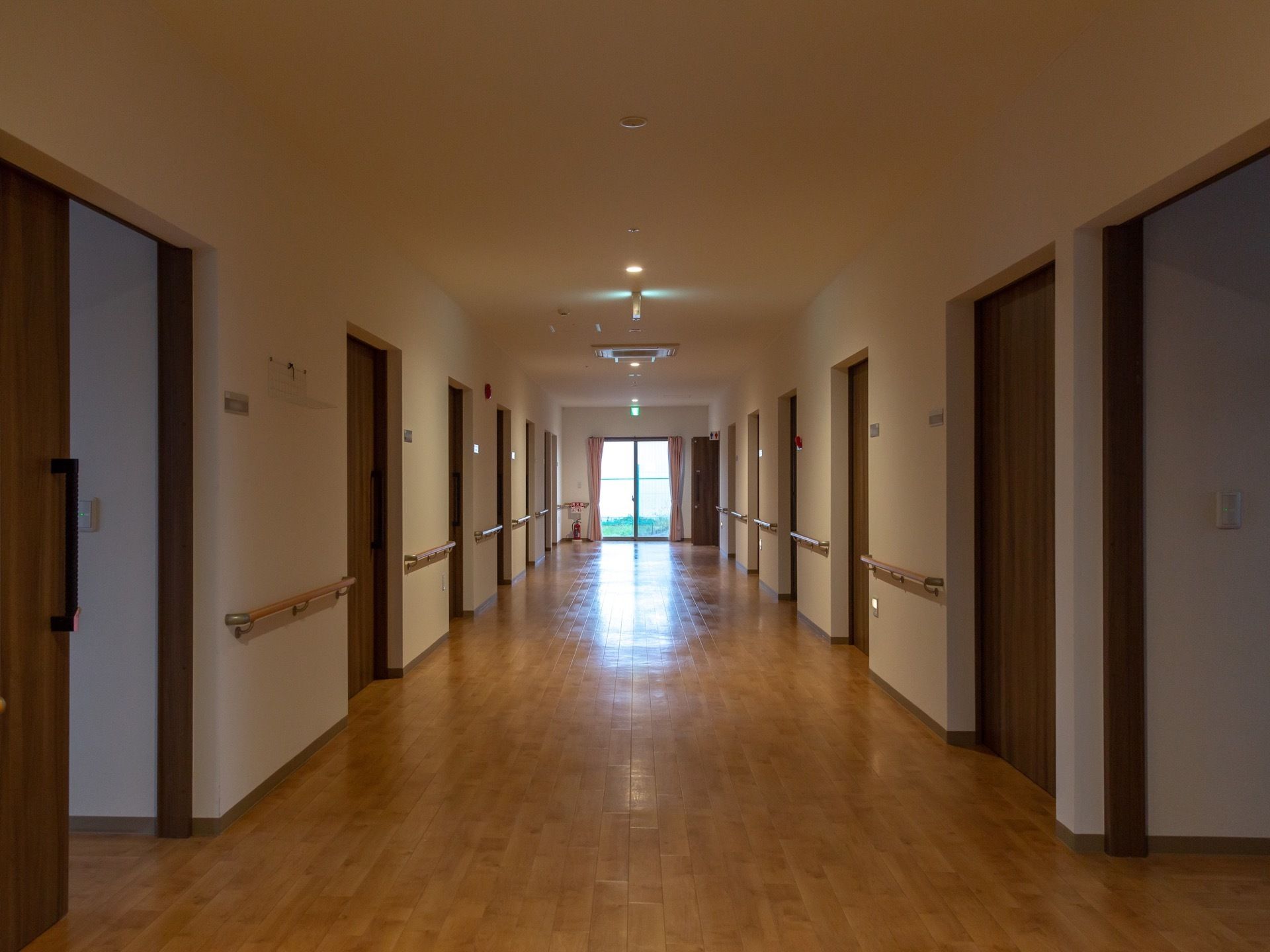 茶色の建具、木目調の床の通路である。落ち着いた雰囲気がただよう。壁の両側には手すりが備えつけられている。