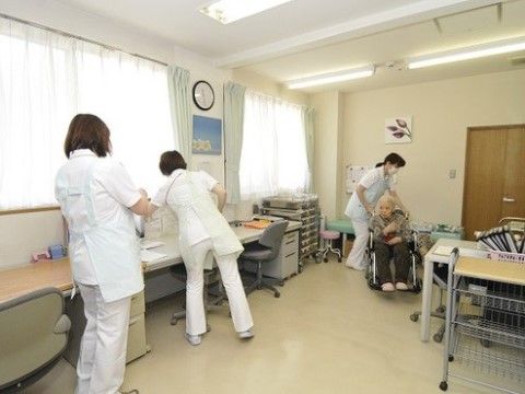 車いすに乗ったご年配の女性を介助する、ナース服を着た女性スタッフ