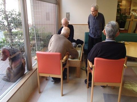 窓際で囲碁をするご年配の男性達と観覧する2人のご年配の男性