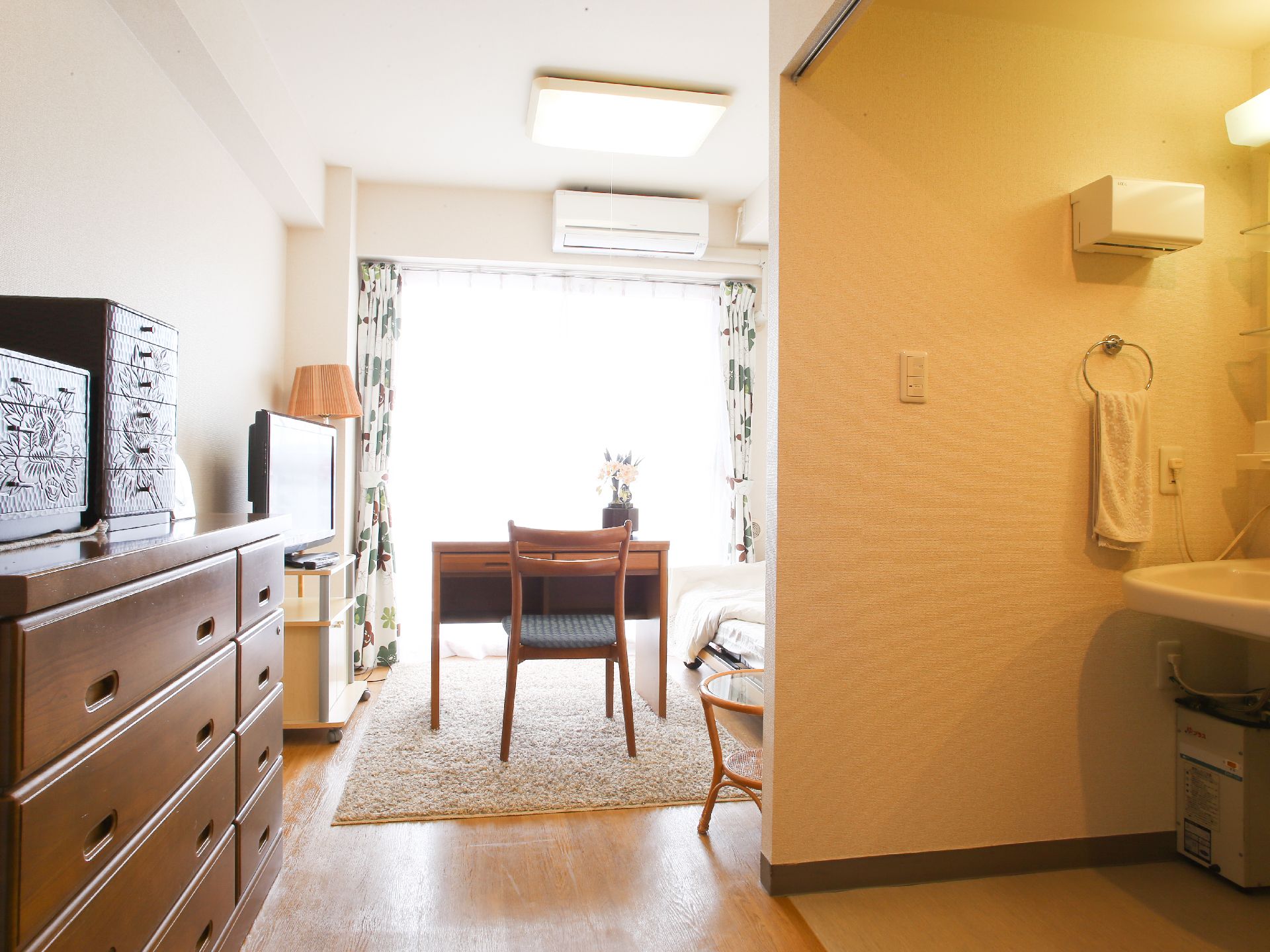 ベッドの部屋の前に洗面台がある。左手には腰の高さより低いタンスがあり、上には小物入れがいくつかのっている。