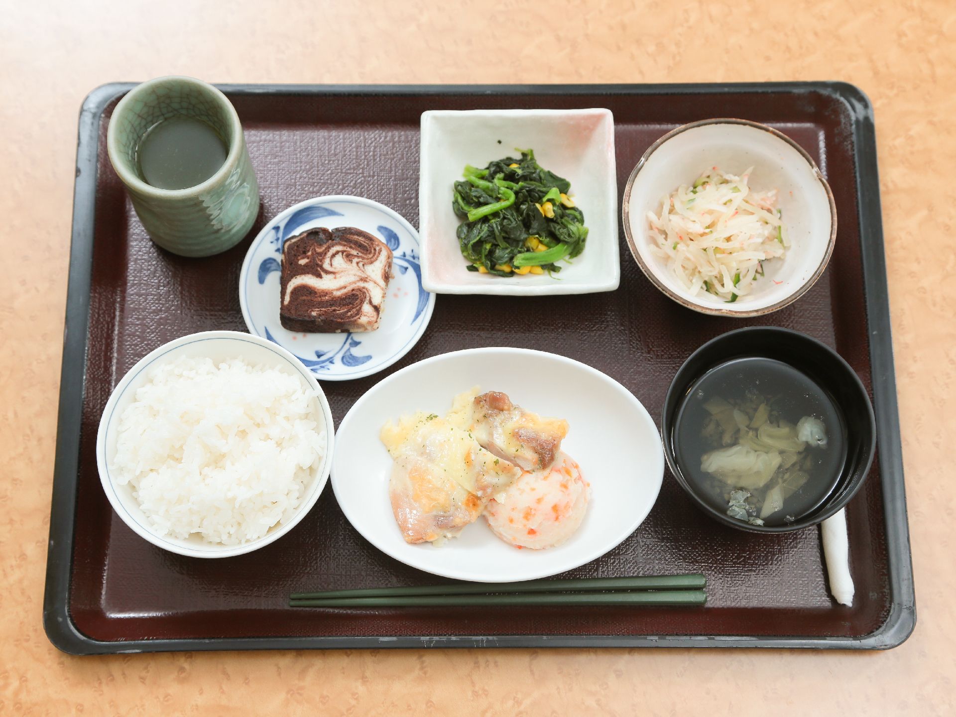 黒い四角いお盆に食事がのっている。ご飯の他にメインとほうれんそうのおひたしなどの副菜とお吸い物、お茶がついている。