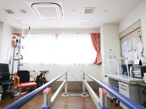 トレーニングルームには歩行を促す機材も設置してある。他にも様々な機材もあり、また右手にはデスクや書類が張り出されてもいる。