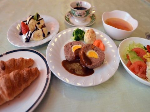 ミートローフとクロワッサン、サラダ、チョコレートシロップが掛かったフルーツ、コーヒーが並んだテーブル