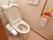 トイレは温水洗浄便座付きで、座って右側にボタンやダイヤルが設置されている。壁には手すりがあり、タオルが掛けられている。