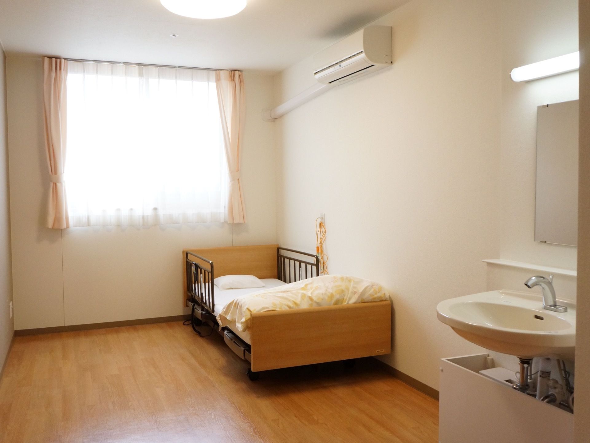 木目調のフローリングの居室は、ぬくもりが感じられる空間である。大きな窓があり、洗面台、エアコンを完備している。