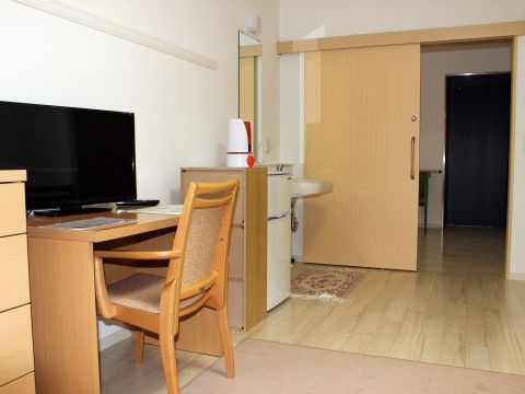 デスクの上にテレビが置かれた、ミニ冷蔵庫の隣に洗面台がある居室