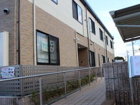 長いスロープのある、ブラウンとベージュ色で落ち着いた配色の施設外観