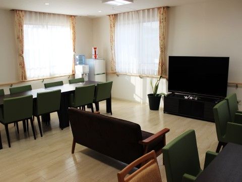 部屋の奥にミニ冷蔵庫とウォータークーラーがある、たくさんの緑の椅子が並べられた共有スペース