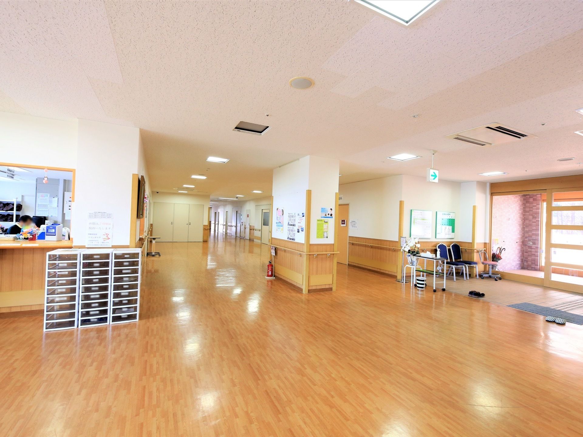 右手に玄関の自動ドアがあり、傘立てと椅子が置かれている。玄関からフロアーまでには段差がない。左手に受付のカウンターが見える。