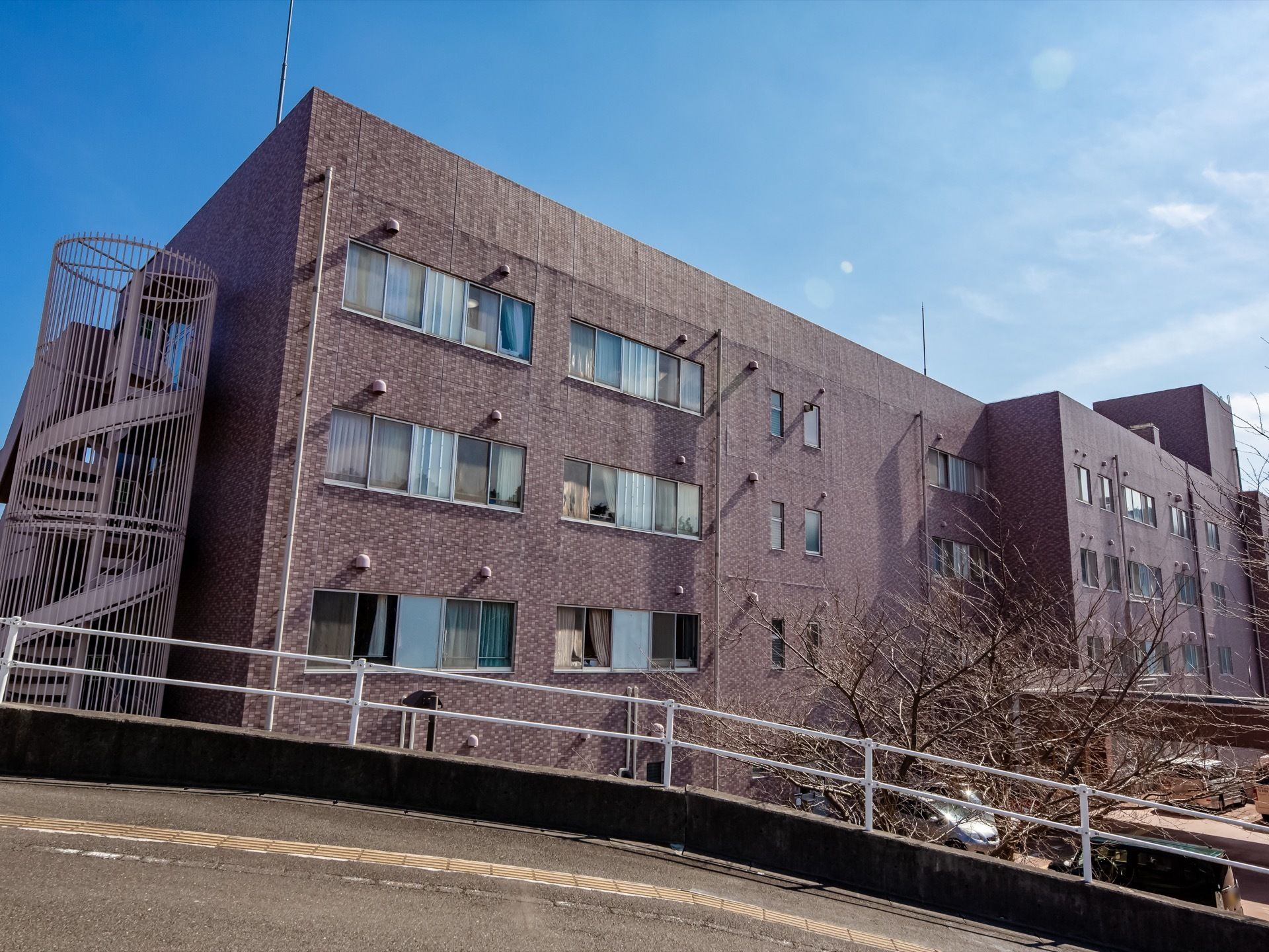 施設横の道は坂道になっており、白いレールが取りつけられている。路面には点字ブロックが設置されている。