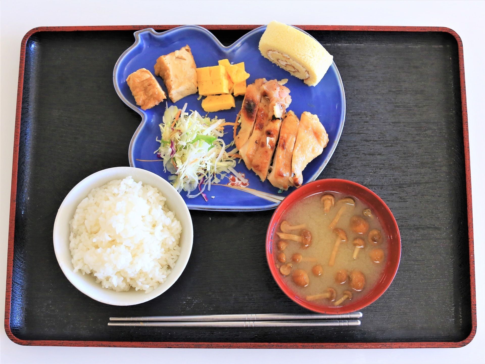 黒いお盆の上に食事が並べられており、青いお皿の上に主菜や副菜、デザートが食べやすい大きさに切られて載せられている。