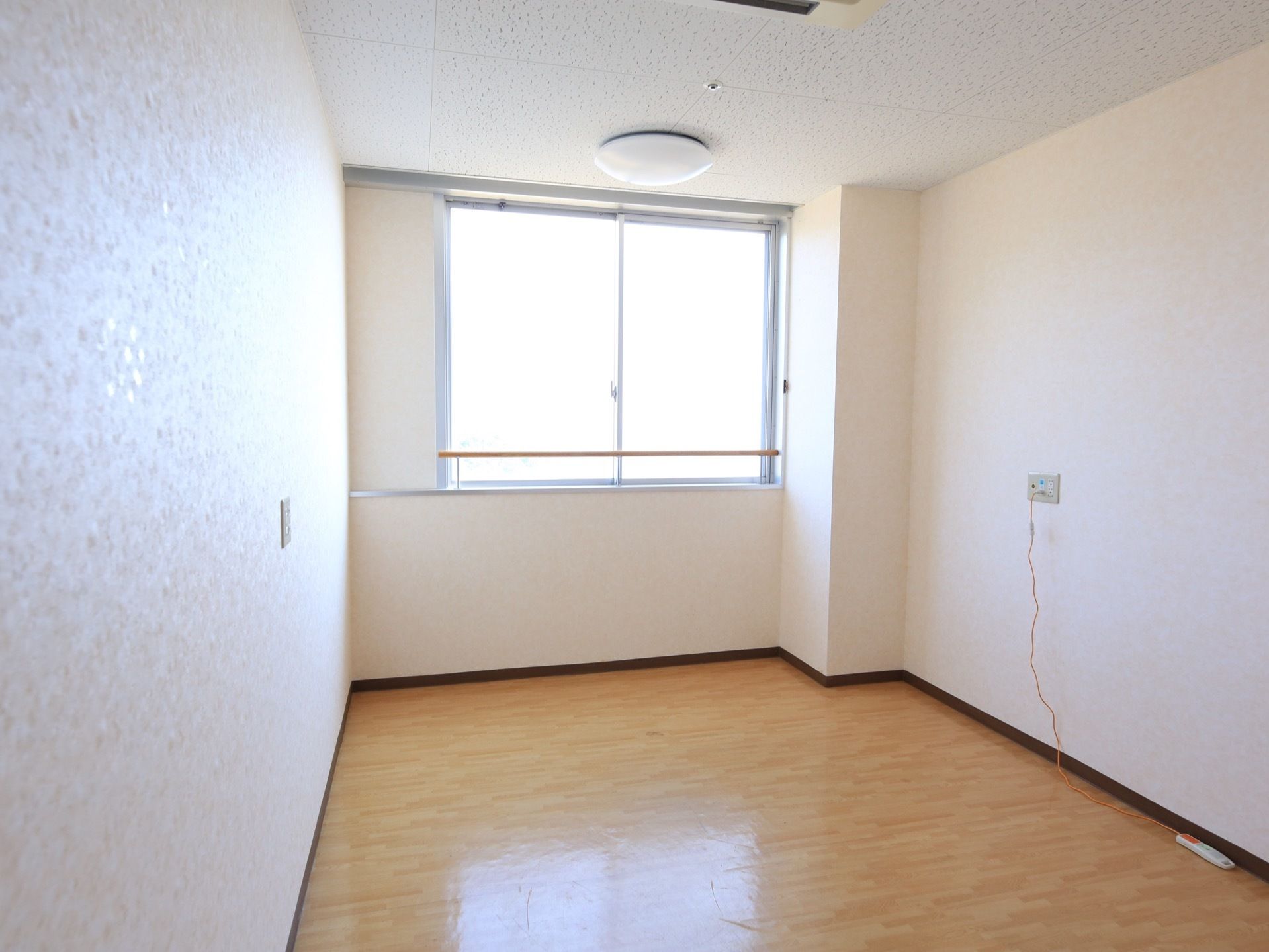 フローリングの居室で、奥に陽当たりの良い腰高窓がある。照明器具、非常呼出ボタンが取りつけられている。