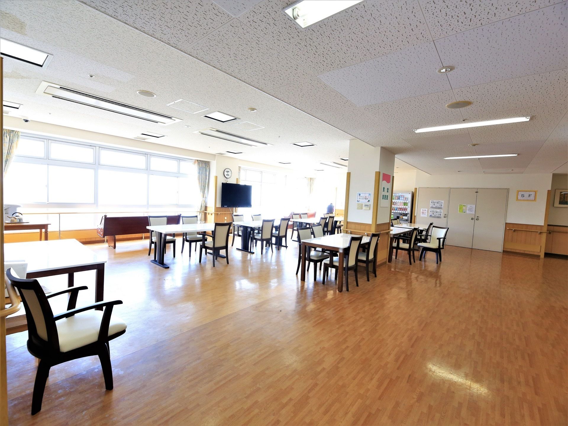 広々とした部屋に、ダイニングテーブルがたくさん置かれている。床は段差や障害物のないフローリングである。