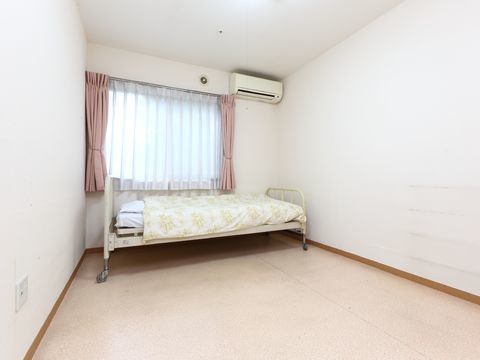 部屋の奥に面する形でベッドが置かれている。壁の半分ほどの窓から日差しが入り込み右上にはエアコンもある。