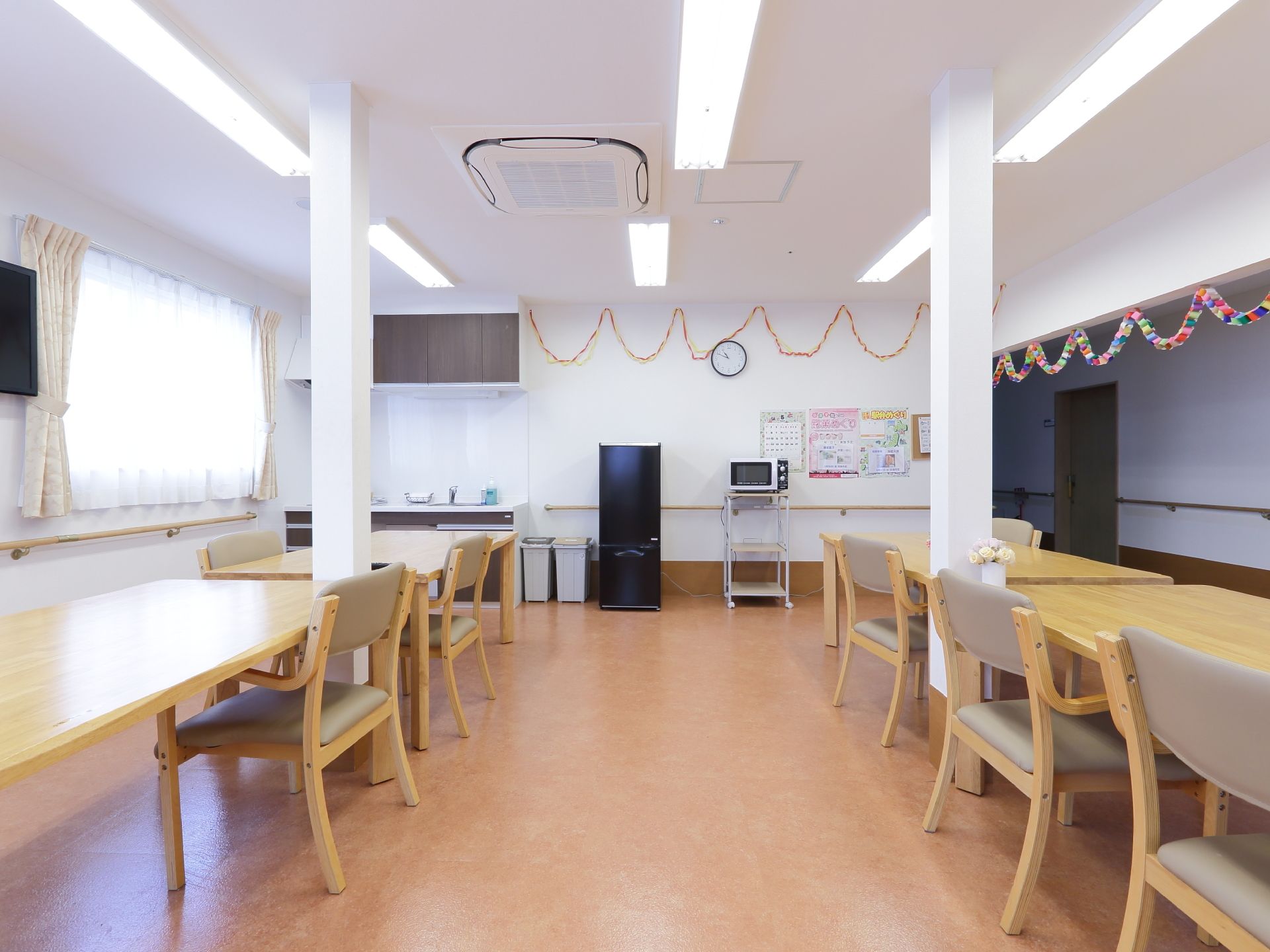 白い壁と天井の部屋に外光の入り込む大きな窓がある。対面式の大きな長テーブルと椅子が配置されており電子レンジもある。