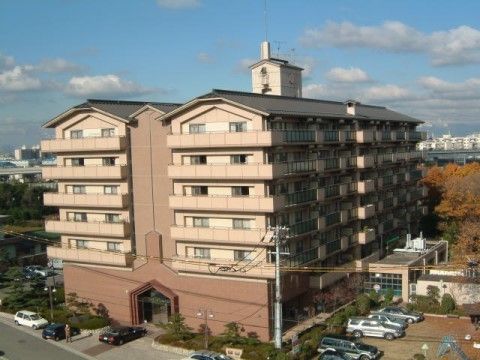 薄い茶色の７階建ての大きな建物である。施設には駐車場も完備している。施設の周りには緑が多く植えられている。