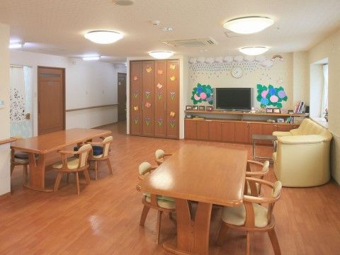 フローリングの広い空間にテーブルと椅子が配置されている。窓際には黄色いソファが、壁際にはテレビがある。