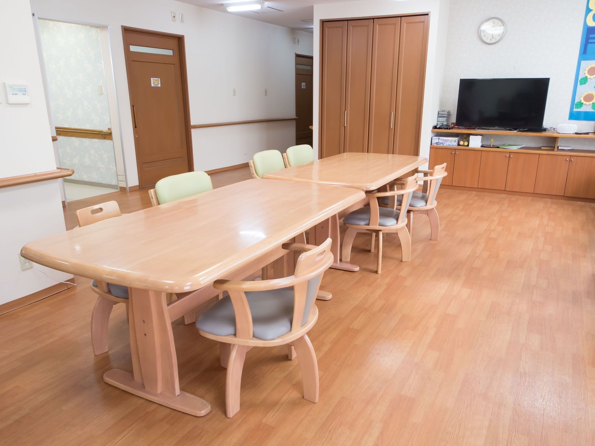 通路との仕切りのない空間に、テーブルと椅子が置かれている。椅子は２種類ある。棚の上にテレビが設置されている。