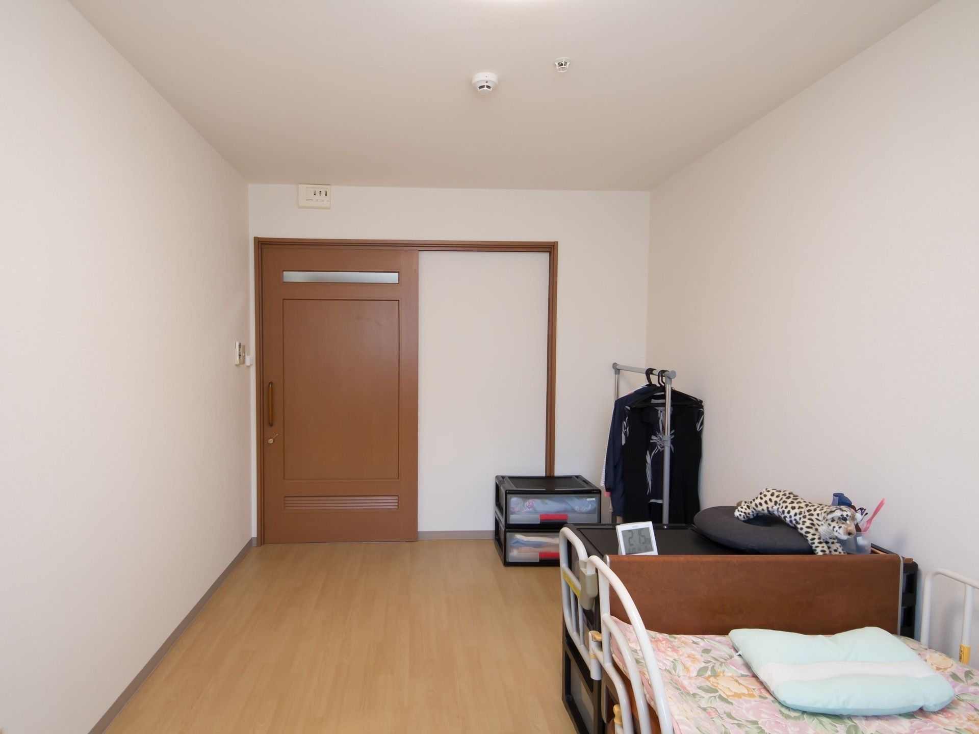 部屋の入口は木目の大きな引き戸となっており、衣装ケースとハンガーラックが置かれ、洋服がかけられている。