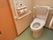 洋式トイレが設置されている。壁にはL字の手すり、便座の壁と反対側にはひじ掛けが設置され背あても付いている。