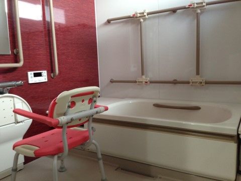 個浴ができる浴室である。壁には様々な形状の手すりが備わっている。洗い場には背もたれと肘掛けが付いた椅子が置かれている。