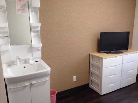 居室内に備わる洗面台である。白色の洗面台は正面に鏡があり、鏡の左右には小物を置くことができる棚が設けられている。