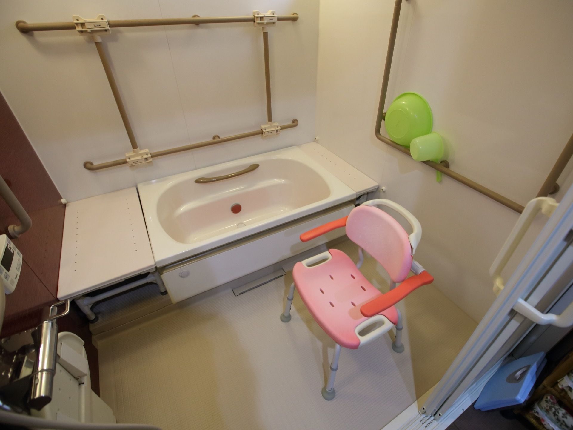 浴室に、ピンク色の背もたれやひじ掛けがついた椅子がある。壁には、縦や横方向の大きな手すりがある。