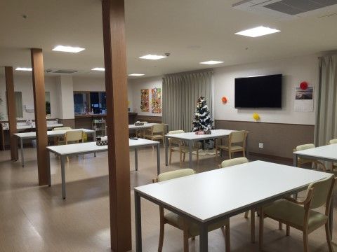 壁掛けテレビとクリスマスツリーがある、ダイニングテーブルがたくさん並んだ食堂