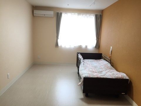 窓の近くに介護用ベッドが置かれた、一面がオレンジのクロスの居室
